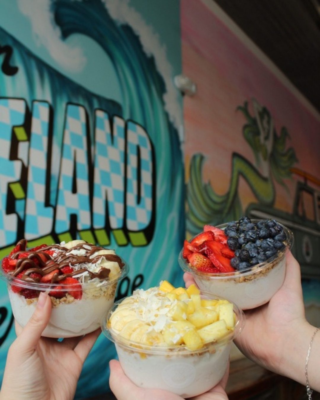 Acai bowls held up in front of a Playa Bowls mural