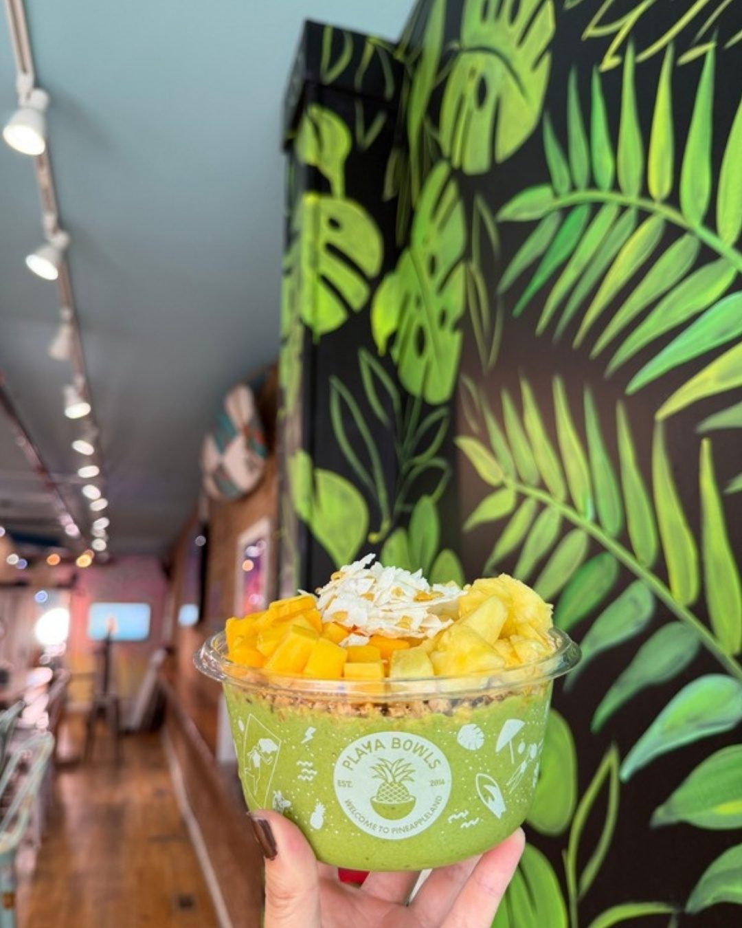 A green bowl topped with mango, pineapple and coconut flakes
