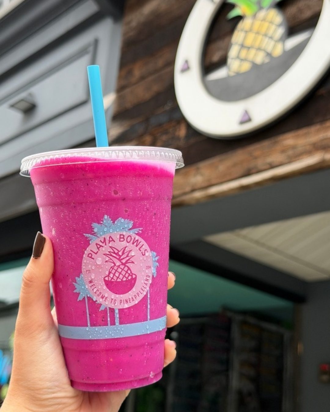 A pink pitaya smoothie in a Playa Bowls cup held up outside
