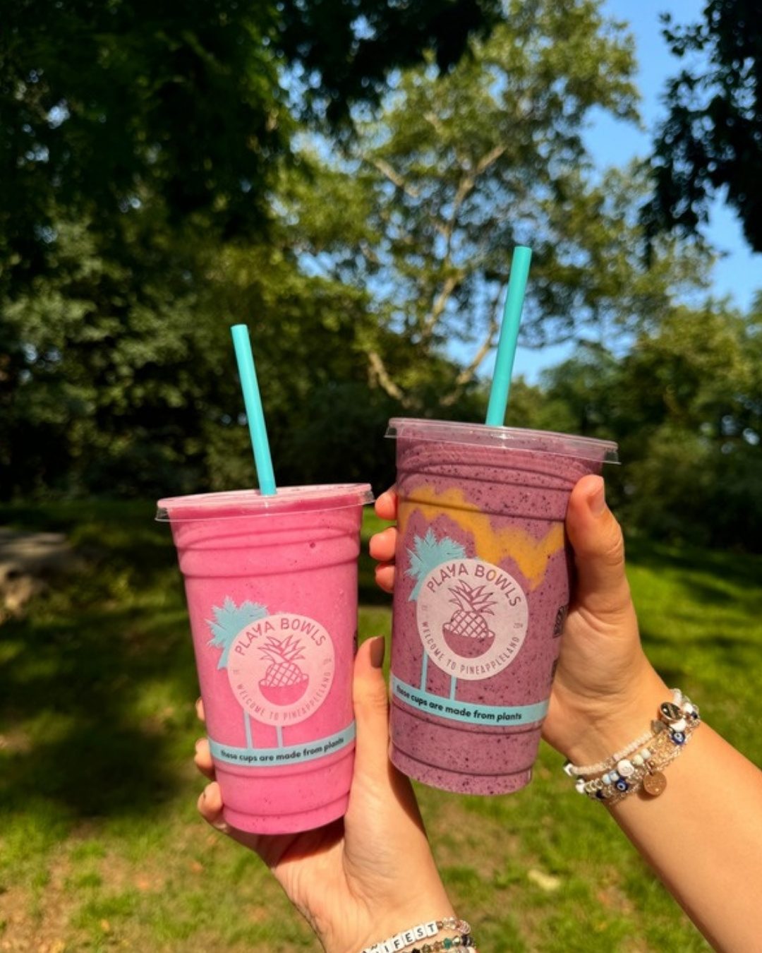 Two Playa Bowls smoothies, one pink and one purple, held up outdoors
